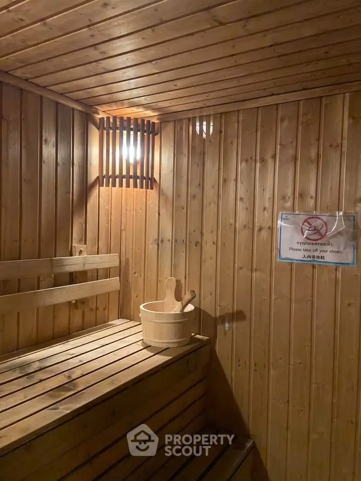 Luxurious wooden sauna room with warm lighting and traditional bucket, perfect for relaxation.