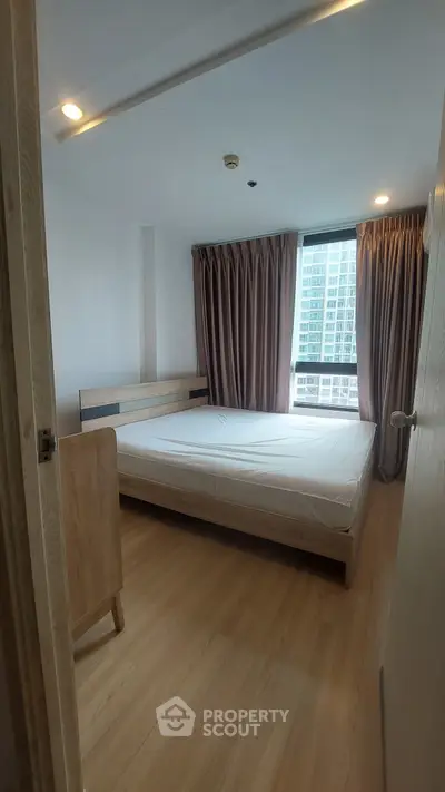 Modern bedroom with large window and wooden flooring in high-rise apartment.