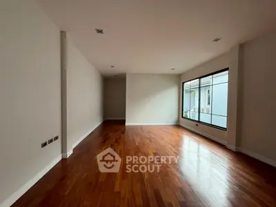 Spacious empty room with wooden flooring and large windows, perfect for customization.