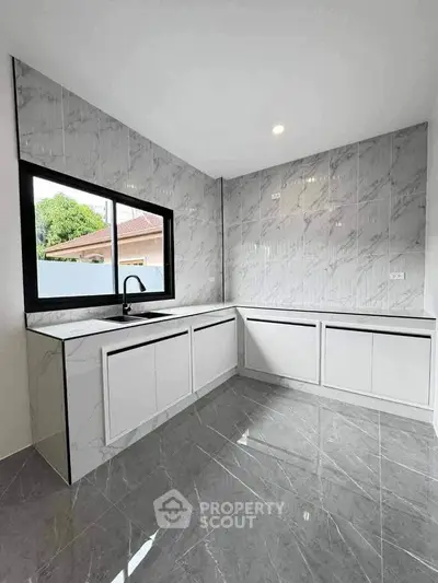 Modern kitchen with sleek white cabinets and marble backsplash, featuring large window for natural light.