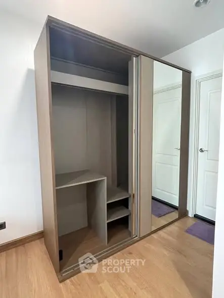Spacious modern wardrobe with sliding mirror doors in a bright room with wooden flooring.