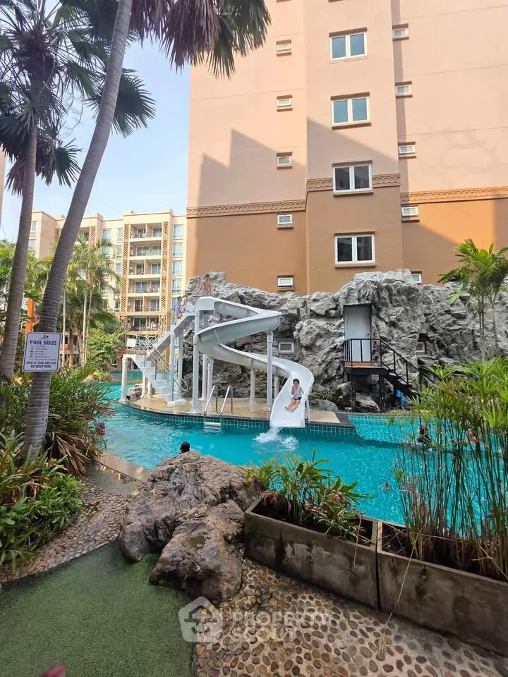 Luxurious apartment complex with stunning pool and water slide, surrounded by lush greenery and modern architecture.