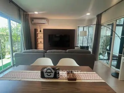 Modern living room with large windows and stylish decor, featuring a cozy seating area and dining table.