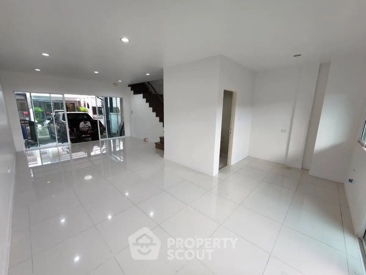 Spacious modern living room with glossy white tiles and large windows for natural light.