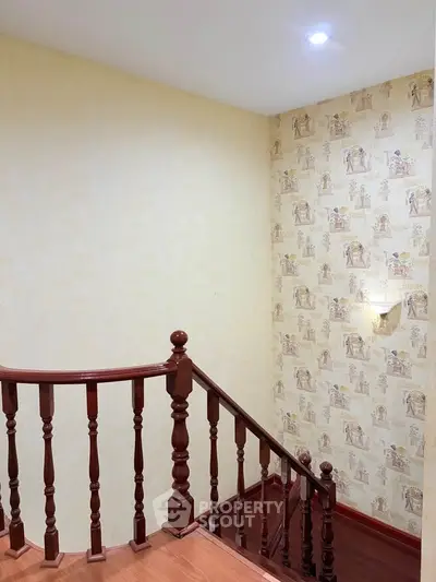 Elegant staircase with wooden railing and vintage wallpaper in a cozy home interior.