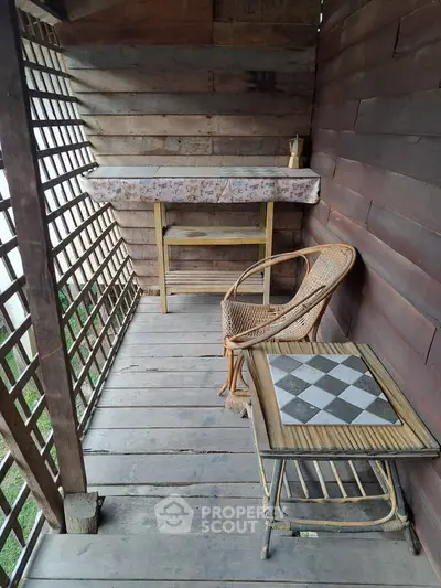 Charming rustic balcony with wooden lattice, wicker chair, and chessboard table, perfect for relaxation.