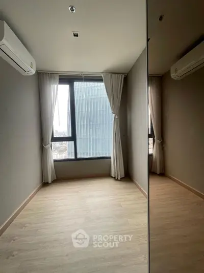 Modern empty room with large window and city view, featuring sleek air conditioning unit.