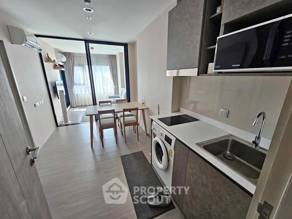 Modern apartment kitchen with dining area and washing machine, featuring sleek design and natural light.