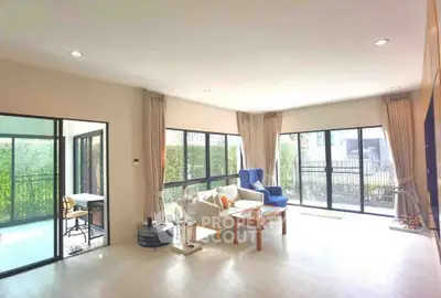 Spacious living room with large windows and garden view, featuring modern furniture and natural light.