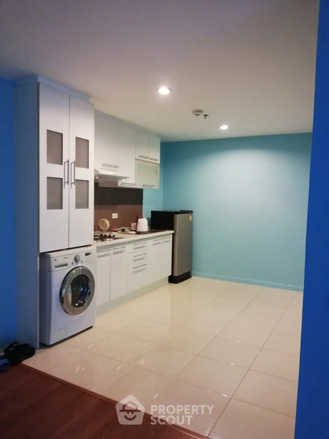 Modern kitchen with washing machine and compact fridge in open layout design.
