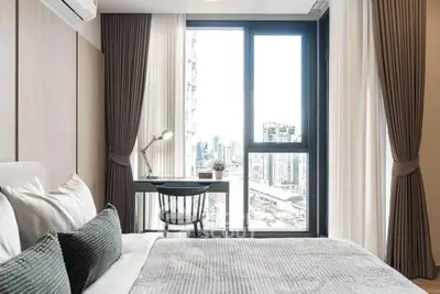 Modern bedroom with city view, featuring elegant decor and a cozy workspace by the window.