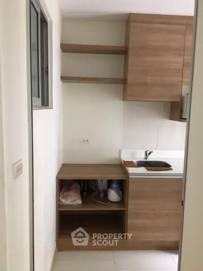 Compact kitchen with wooden cabinets and open shelving in modern apartment.