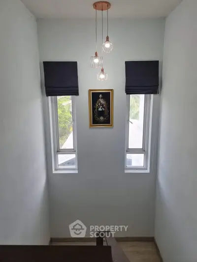 Elegant stairway with modern lighting and framed art between two windows.