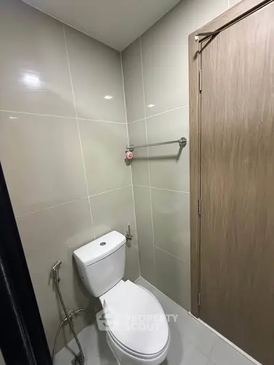 Modern bathroom with sleek design and neutral tiles, featuring a toilet and towel rack.