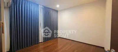 Spacious empty room with wooden flooring and blue curtains, ideal for customization.