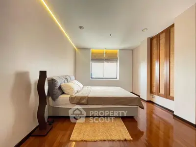 Spacious bedroom with modern design and wooden flooring, featuring a cozy bed and ambient lighting.