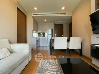 Modern open-plan living room with sleek kitchen and dining area, featuring elegant furnishings and wooden flooring.
