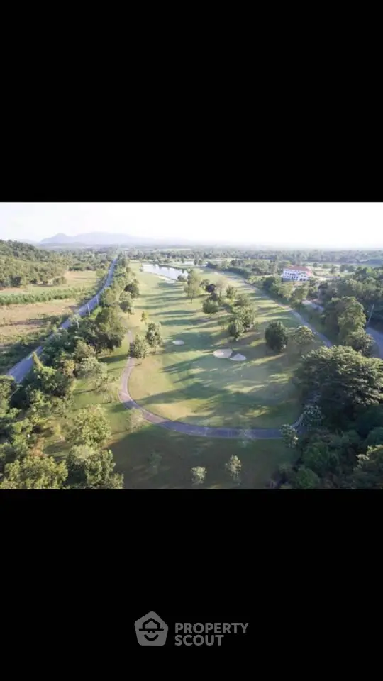 Scenic aerial view of lush golf course surrounded by greenery and distant hills, perfect for luxury real estate.