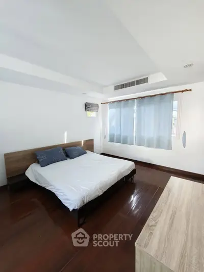 Spacious bedroom with wooden flooring and large window for natural light