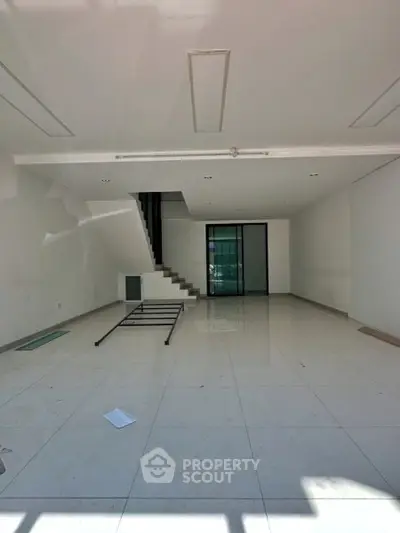 Spacious modern living room with sleek staircase and large windows, perfect for natural light and open living.