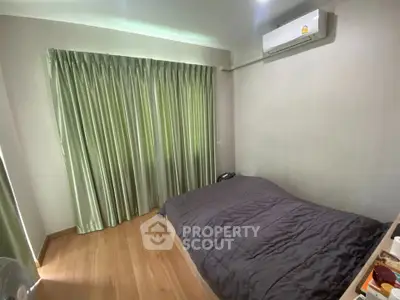 Cozy bedroom with wooden flooring and air conditioning, featuring green curtains for a serene ambiance.