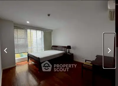 Spacious bedroom with wooden flooring and large window for natural light.