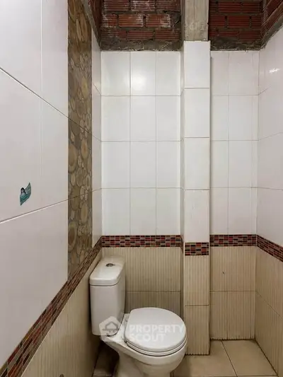 Compact bathroom with tiled walls and modern toilet in a real estate property.