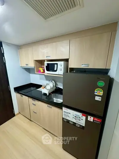 Modern kitchen with sleek cabinets, microwave, and fridge in compact layout.
