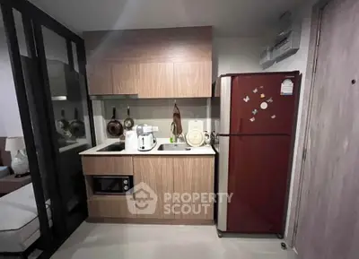 Modern compact kitchen with wooden cabinets and red fridge in cozy apartment.