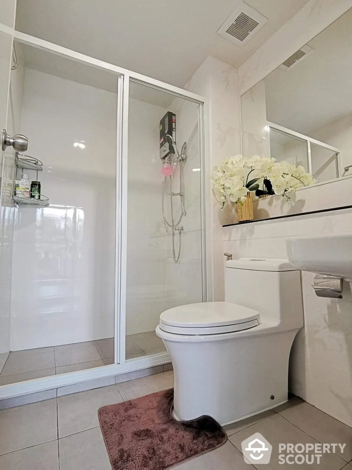 Pristine white bathroom with glass-enclosed shower and modern fixtures, accented by a vibrant floral arrangement for a touch of elegance.