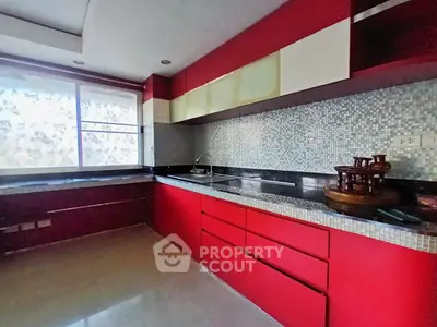 Modern kitchen with red cabinetry and mosaic backsplash, featuring sleek countertops and ample natural light.