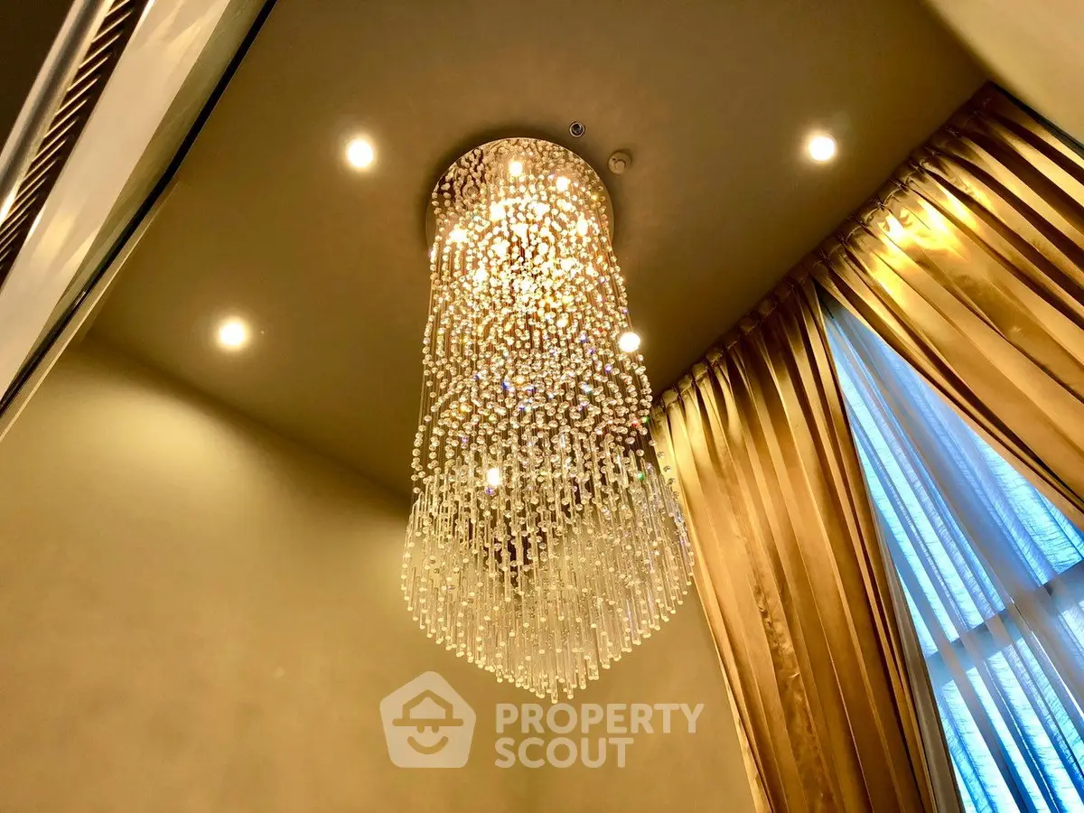 Luxurious chandelier in elegant living room with high ceiling and golden drapes