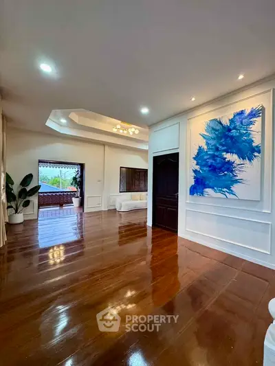 Spacious living room with elegant wooden flooring and modern art, opening to a large balcony with scenic views.