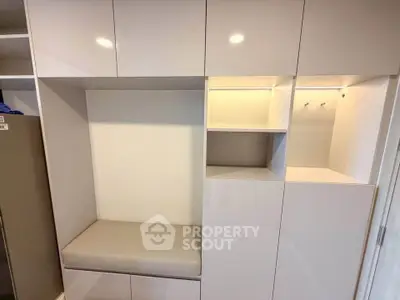 Modern built-in storage unit with sleek white cabinets and cushioned seating area.