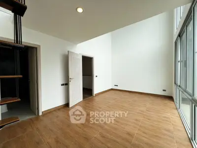 Spacious modern living room with high ceilings and wooden flooring, featuring large windows for natural light.