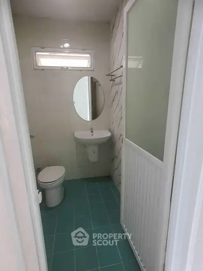 Compact bathroom with modern fixtures and teal floor tiles, featuring a round mirror and a shower enclosure.