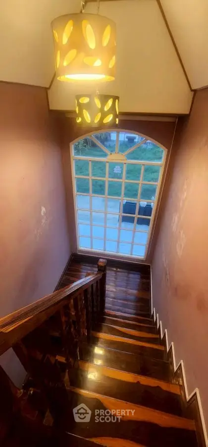 Charming wooden staircase with elegant lighting and large window view.