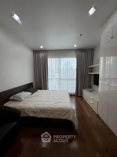 Modern bedroom with wooden flooring and large window in a stylish apartment.