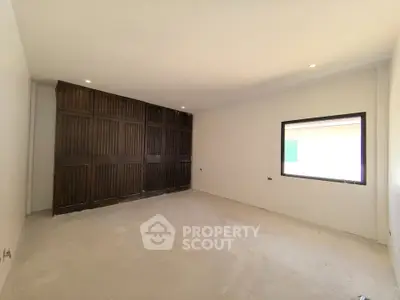 Spacious unfurnished room with large window and wooden accent wall, ideal for customization.