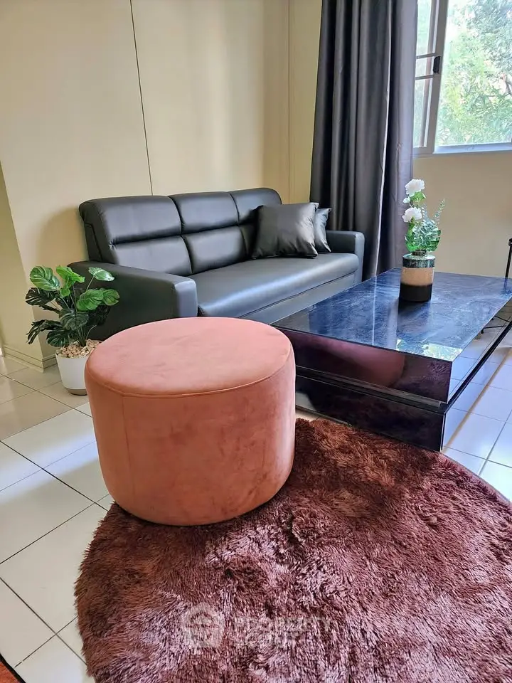 Modern living room with sleek black sofa, plush pink ottoman, and stylish decor for a cozy ambiance.