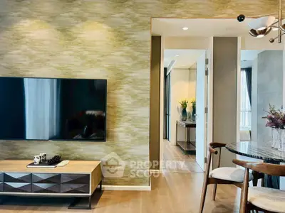 Modern living room with stylish decor and large TV, open to a bright hallway.