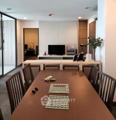 Modern dining area with wooden table and chairs, open layout leading to cozy living room with TV.