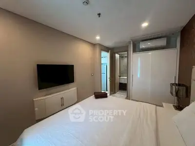 Modern bedroom with wall-mounted TV and ensuite bathroom in stylish apartment.