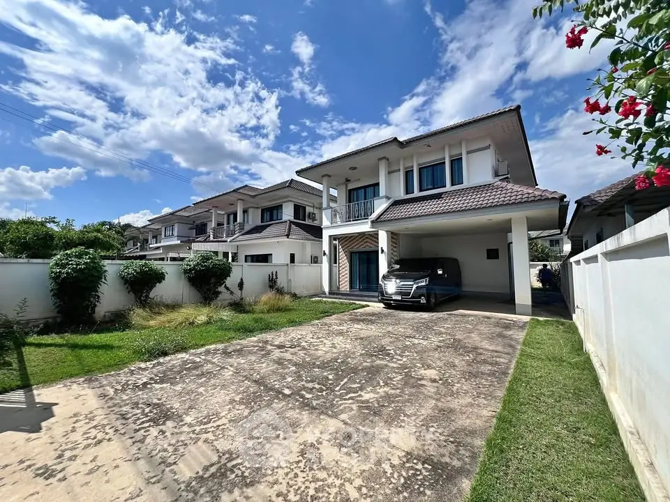 Charming two-story house with spacious driveway and lush garden under a clear blue sky.