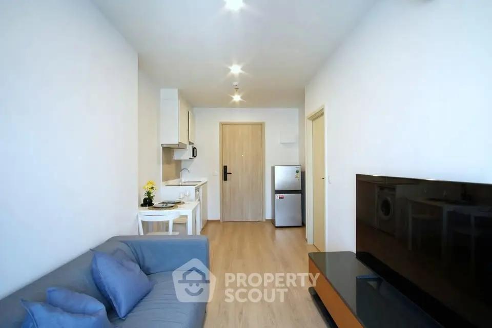 Modern living room with sleek design, featuring a cozy sofa, flat-screen TV, and compact kitchen area.