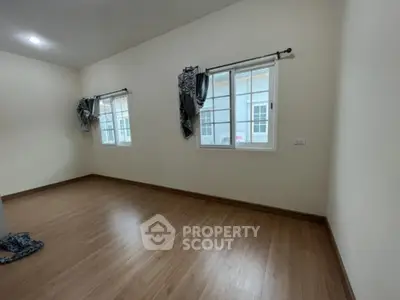 Spacious empty room with wooden flooring and large windows for natural light.