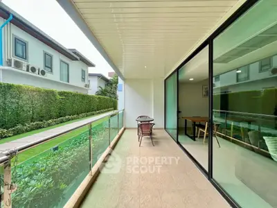 Spacious balcony with glass railing overlooking lush garden in modern residential complex.