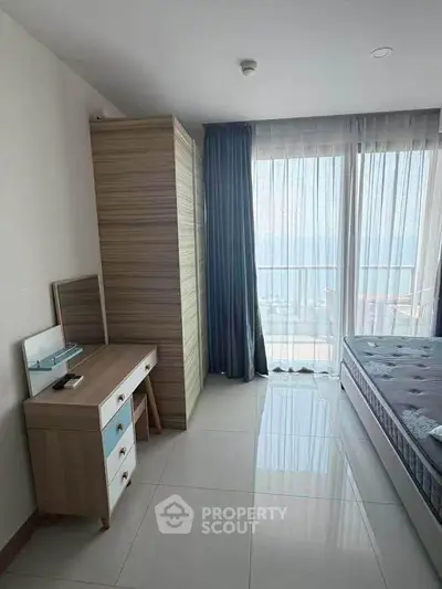 Bright bedroom with ocean view, featuring a cozy bed, stylish dresser, and floor-to-ceiling windows.
