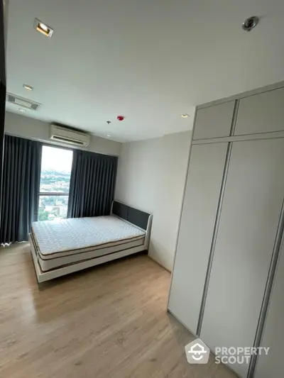 Modern bedroom with large window and city view, featuring sleek wardrobe and minimalist design.