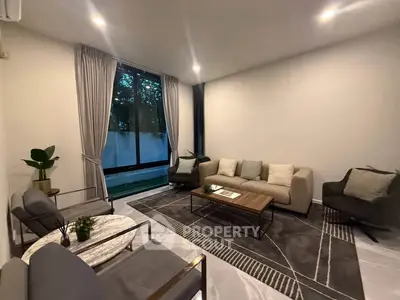 Elegant living room with modern furniture and large window offering serene garden view.